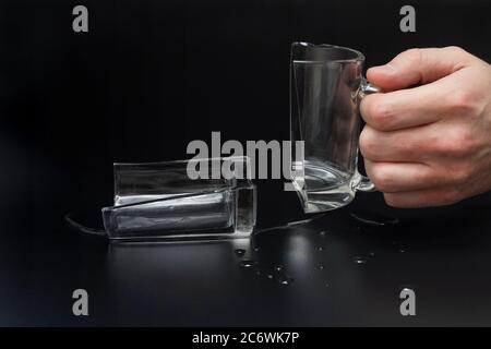 Man holds broken glass cup on black background, incident concept Stock Photo