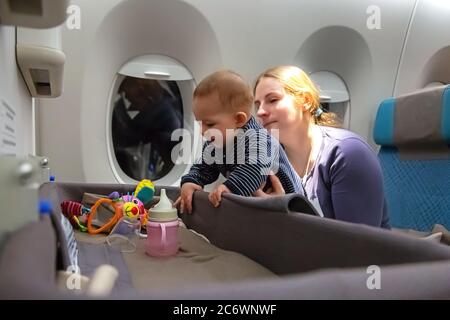 Infant plays on mother hands at the airplane. Interest to special baby bassinet during the flight Stock Photo