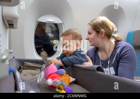 Interest to special baby bassinet during the flight. First flight of infant girl. mother holds baby in her arms in plane Stock Photo