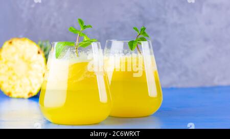 Pineapple juice on a blue gray background. Juice for detox in the glass. Pineapple smoothie with fresh pineapple. Summer drink with mint Stock Photo