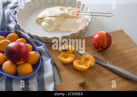 Cooking homemade apricot pie. Slices of fresh apricots for pie on a cutting board, dough in a white baking dish. Stock Photo