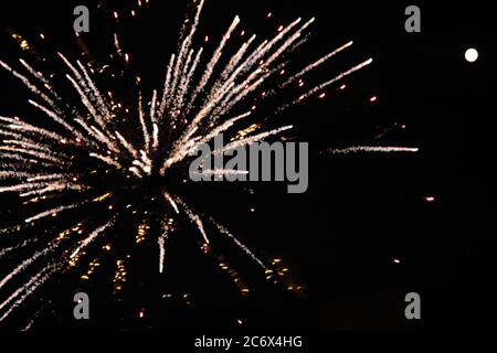 a close up single explosion of a spider rocket firework with a full moon to the side from a new york city rooftop against a night sky Stock Photo