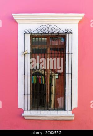 Colonial style architecture with a pink wall and wrought iron decoration on wooden window, Oaxaca, Mexico. Stock Photo