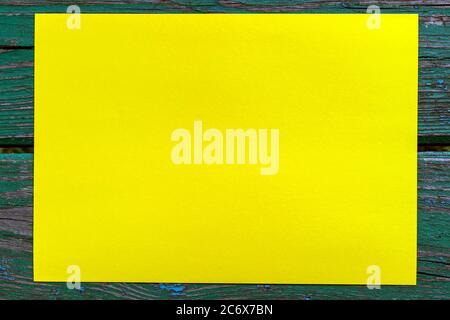 Blank yellow paper on green wooden surface. Template, wallpaper, poster, postcard, background. Top view, copy space, close up Stock Photo