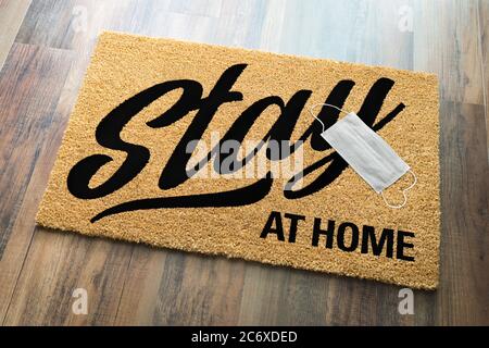 Stay At Home Welcome Mat with Medical Face Face Resting On Floor. Stock Photo