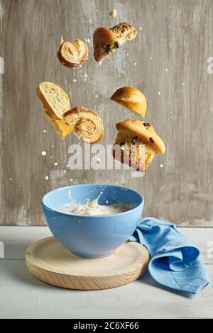 blue bowl with wooden plate and blue napkin with splashes of milk flying chocolate muffins, palm tree,and milk bun on a rustic grey background. food a Stock Photo