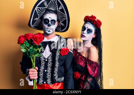 Young couple wearing mexican day of the dead costume holding roses thinking attitude and sober expression looking self confident Stock Photo