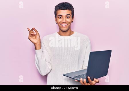 Young african amercian man holding laptop smiling happy pointing with hand and finger to the side Stock Photo