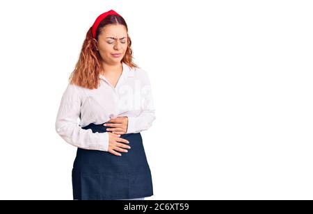 Young latin woman wearing waitress apron with hand on stomach because indigestion, painful illness feeling unwell. ache concept. Stock Photo