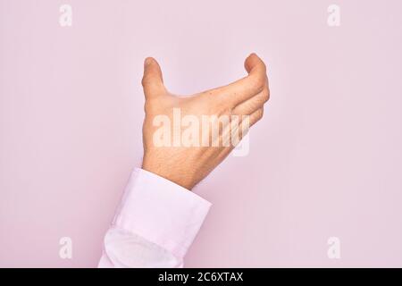 Hand of caucasian young man showing fingers over isolated pink background holding invisible object, empty hand doing clipping and grabbing gesture Stock Photo