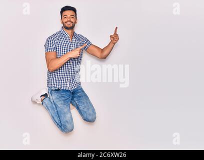 Young handsome hispanic man wearing casual clothes smiling happy. Jumping with smile on face pointing with fingers to the side over isolated white bac Stock Photo