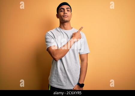 Handsome african american sportsman doing sport wearing sportswear over yellow background Pointing with hand finger to the side showing advertisement, Stock Photo