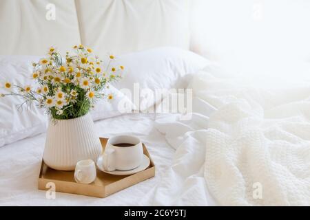Cozy breakfast in bed, cup of coffee and milk on the grey fabric, space for text. Alarm clock for seven in the morning. Stock Photo
