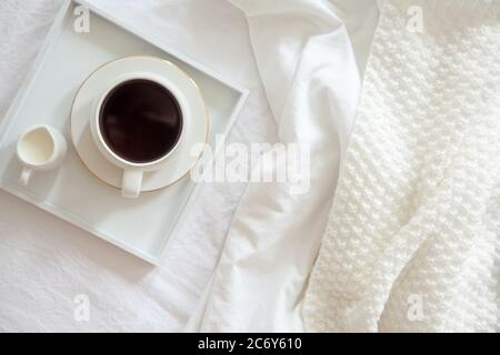 Cozy breakfast in bed, cup of coffee and milk on the grey fabric, space for text. Alarm clock for seven in the morning. Stock Photo
