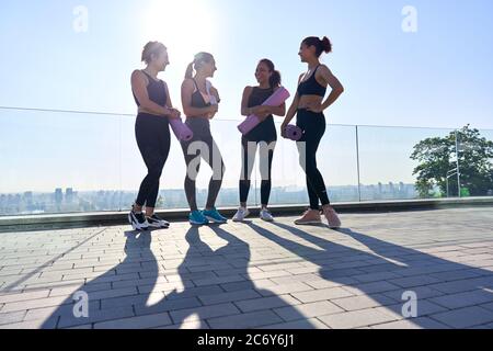 Happy diverse fit girls friends laugh stand hold mats group yoga class outdoor. Stock Photo