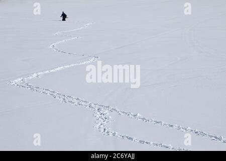 A male fisherman , far away , wading on deep snow on lake ice at Winter , Finland Stock Photo