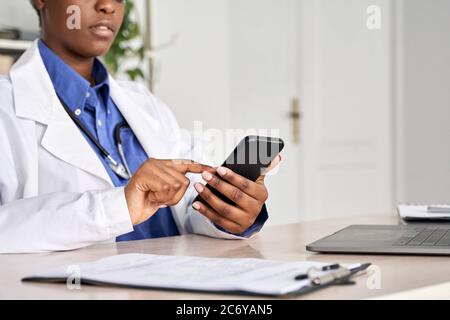 African female doctor holding in hands using smart phone, close up view. Stock Photo