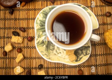 A Cup of tea, dried rosehip fruit, pieces of brown cane sugar, and cookies on a reed Mat. Close up Stock Photo