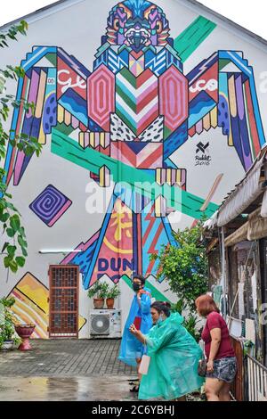 Thai tourists taking photos in front of a large and colorful wall painting in Thalang Road in the Old Town area (Chinatown) of Phuket Town,, Thailand Stock Photo