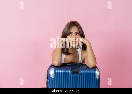 Frustrated young woman waiting to go on vacation with elbows on luggage against plain pink background Stock Photo