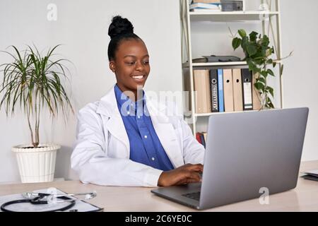 Smiling african american female doctor gp using laptop computer at workplace. Stock Photo