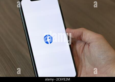 Person using a cellphone with the Facebook icon logo on-screen. Stock Photo