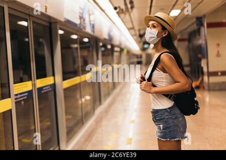 Young Hispanic Brunette woman wearing protective face covering standing on station platform Stock Photo