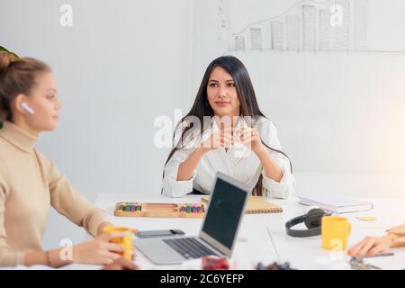 Young business ladies interacting during coffee break at business conference in white office, fruits and cup of tea on table. women colleague gathered Stock Photo