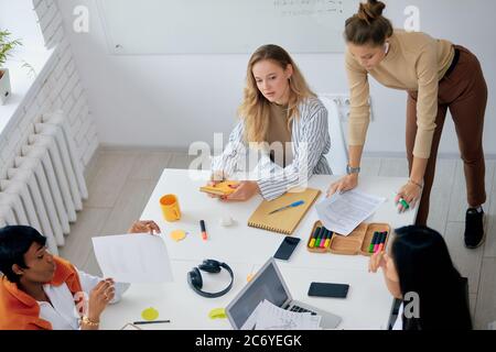Young modern caucasian and african businesswomen presenting meeting in light office, using modern technologies, discuss and explain. Business coworkin Stock Photo
