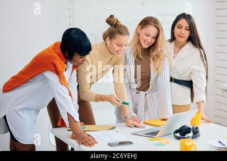 Creative female managers, female teamwork of diverse people in modern white office using laptop. Success depends on togetherness and teamwork Stock Photo