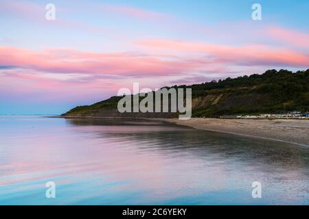 Lyme Regis, Dorset, UK.  13th July 2020.  UK Weather.  Clouds glow pink above Monmouth Beach at Lyme Regis in Dorset at sunrise.  Picture Credit: Graham Hunt/Alamy Live News Stock Photo