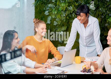Confident young african lady in white shirt stand talking to caucasian young women, teaching business mentoring, discuss strategy in modern office Stock Photo
