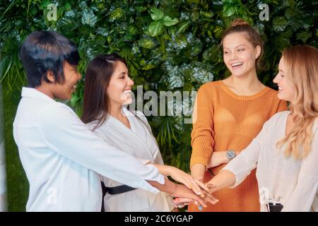 Young multi-ethnic business team celebrate their win, putting hands together, joined hands in office Stock Photo