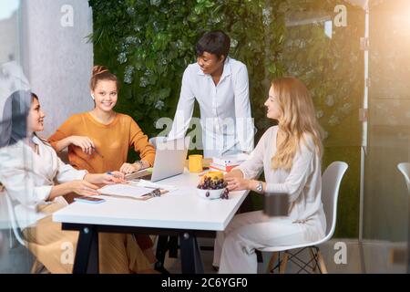 successful good-looking african female giving speech to caucasian women working as team, attentive listeners of african coach teacher leader Stock Photo