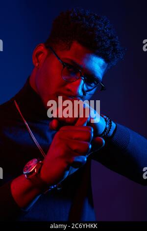 Young handsome Afro-american guy in spectacles and rollneck sweater standing as boxer in defense stance against dark violet background Stock Photo