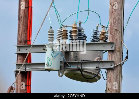 A high voltage transformer reducing the overhead line voltage to supply domestic properties in a rural location with the electrical works high up. Stock Photo