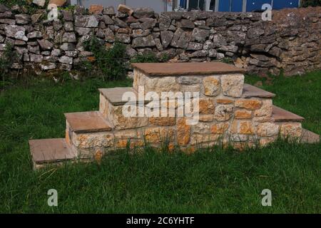A newly made set of steps to aid persons getting onto their horses situated along the roadside next to a large farm building which houses horses. Stock Photo