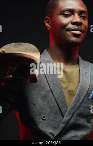 Portrait of energetic, sporty, self-assured handsome african man infashionable blazer suit holding longboard in hands, posing isolated in studio on da Stock Photo