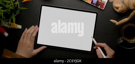 Top view of female designer drawing on mock up tablet with stylus pen on worktable with painting tools Stock Photo