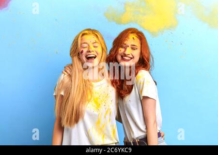 funny mad girls enjoying the festival of spring, colours and love. isolated blue background, studio shot. joy concept. amusing yellow smoke