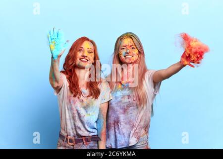 cheerful awesome funny female friends throwing colorful powder at holi festival. isolated blue background, studio shot. great time Stock Photo