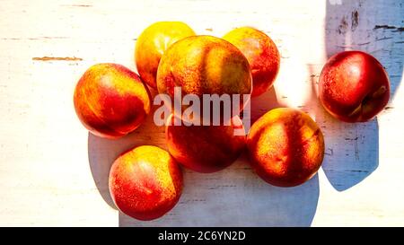 Ripe peaches with leaves on an old wooden table on a background of green leaves in the garden. Soft selective focus Stock Photo