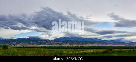 Panorama of a mountain valley in the summer, cloudy sky. Fairytale sunset over the mountain peaks, amazing nature, summer in the mountains. Travel. be Stock Photo