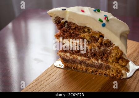 A piece of chocolate sponge cake with cream close up decorated with multicolored topping on a wooden board Stock Photo
