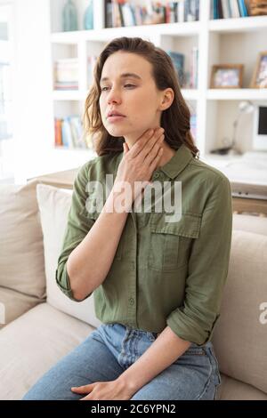 Woman with sore throat holding her neck at home Stock Photo