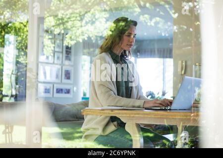 Woman using laptop while sitting near the window at home Stock Photo