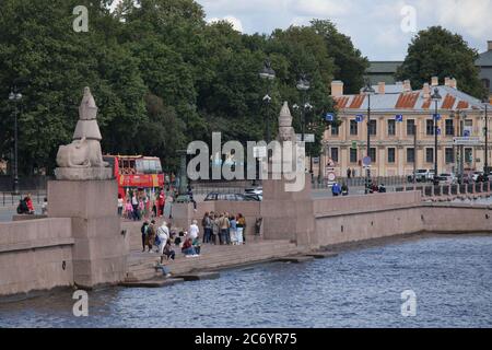 St. Petersburg, Russia - July 12, 2020: People resting at Neva river near the Egyptian sphinxes at the Academy of Fine Arts. Ancient statues was installed here in 1834 Stock Photo