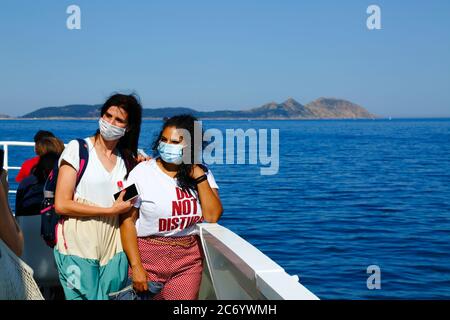 12th July 2020, Ria de Vigo, Galicia, northern Spain: Passengers wearing face masks pose for a photo on the ferry from Vigo to the Cies Islands (in background), a popular tourist destination off the coast of Galicia. Spain has relaxed travel restrictions from 21st June after a strict lockdown to control the Covid 19 coronavirus and many Spaniards are returning to the beaches. Wearing face masks is still mandatory on public transport. Stock Photo