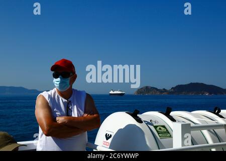 12th July 2020, Ria de Vigo, Galicia, northern Spain: A passenger wearing a face mask on the ferry from Vigo to the Cies Islands (in background), a popular tourist destination off the coast of Galicia. Spain has relaxed travel restrictions from 21st June after a strict lockdown to control the Covid 19 coronavirus and many Spaniards are returning to the beaches. Wearing face masks is still mandatory on public transport. Stock Photo