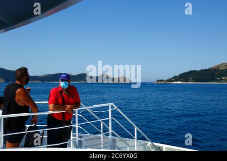 12th July 2020, Ria de Vigo, Galicia, northern Spain: Passengers wearing face masks on the ferry from Vigo to the Cies Islands (in background), a popular tourist destination off the coast of Galicia. Spain has relaxed travel restrictions from 21st June after a strict lockdown to control the Covid 19 coronavirus and many Spaniards are returning to the beaches. Wearing face masks is still mandatory on public transport. Stock Photo